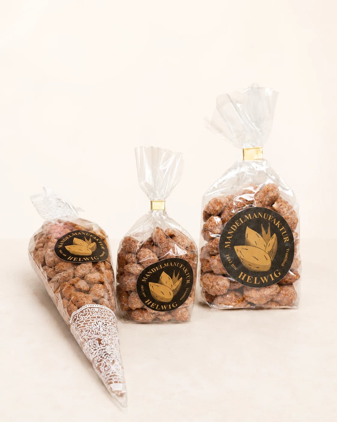 Übersicht der drei Verpackungen der Mandelmanufaktur Helwig — 100 g und 200 g Bodenbeutel sowie 200 g Spitztüte, jeweils mit rundem Helwig-Sticker